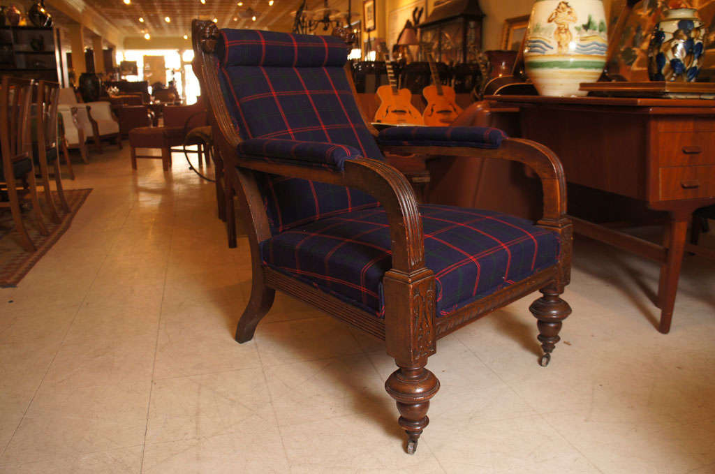 Late 19th century library chair in oak, carved with lion head finials, reeded arms, and bold turned legs with original casters.  Newly upholstered in dark blue tartan Quadrille fabric