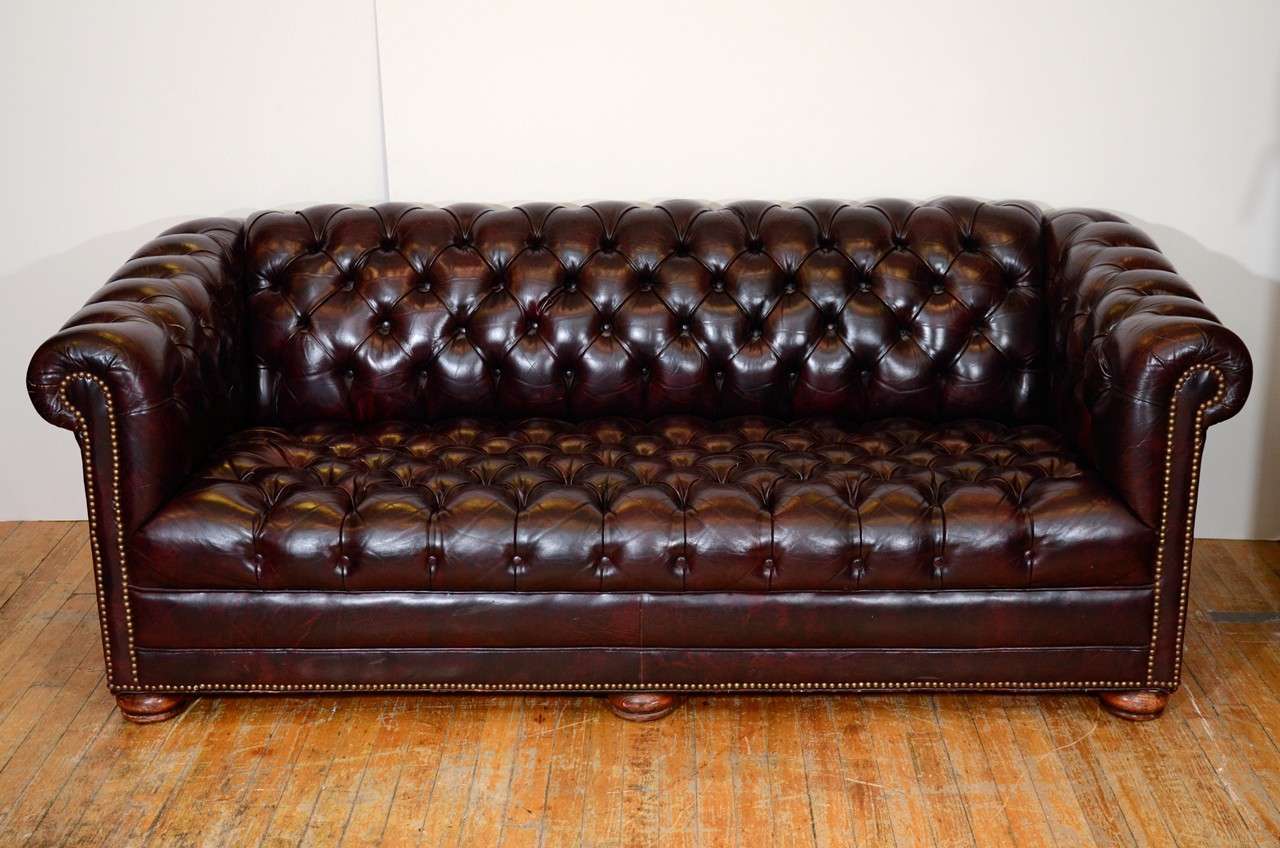A vintage Mid Century button tufted classic Chesterfield sofa in a deep oxblood red leather with brass nail head trim. The piece is in good vintage condition with age appropriate wear; some scratches to leather commensurate with age and