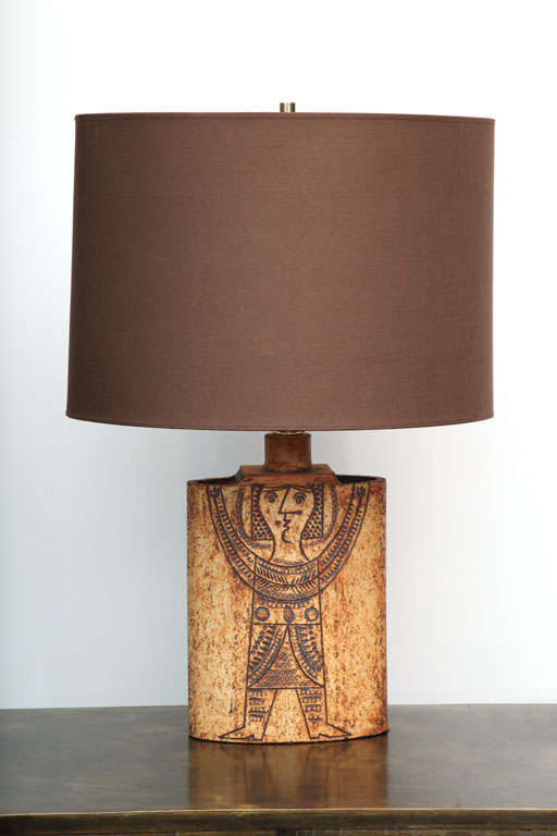 Earthenware lamp with incised, figural decoration and rough ceramic texture. Elliptical fabric shade, signed on back.