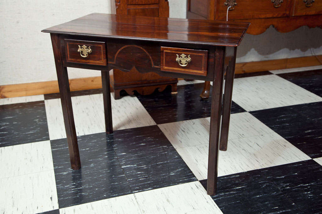 This delightful table has a dark finish that accentuates the bit of boxwood stringing decorating the drawer fronts and center face. A bit of shaping to the apron gives this little country table a bit of panache normally associated with its more