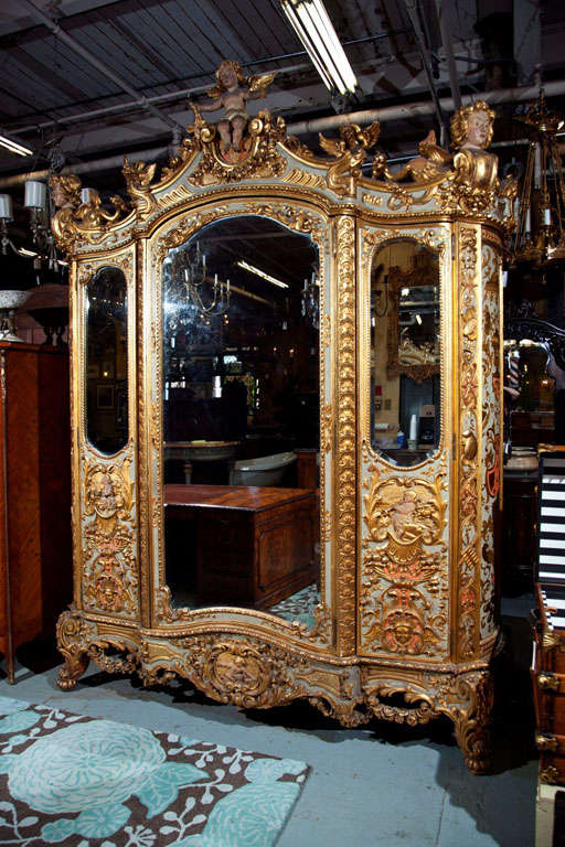 Palatial three door Baroque Style Gilt and painted armoire.
Carved figures of cherubs, musical instruments and birds eye maple interior. Original Beveled mirrors in great shape.