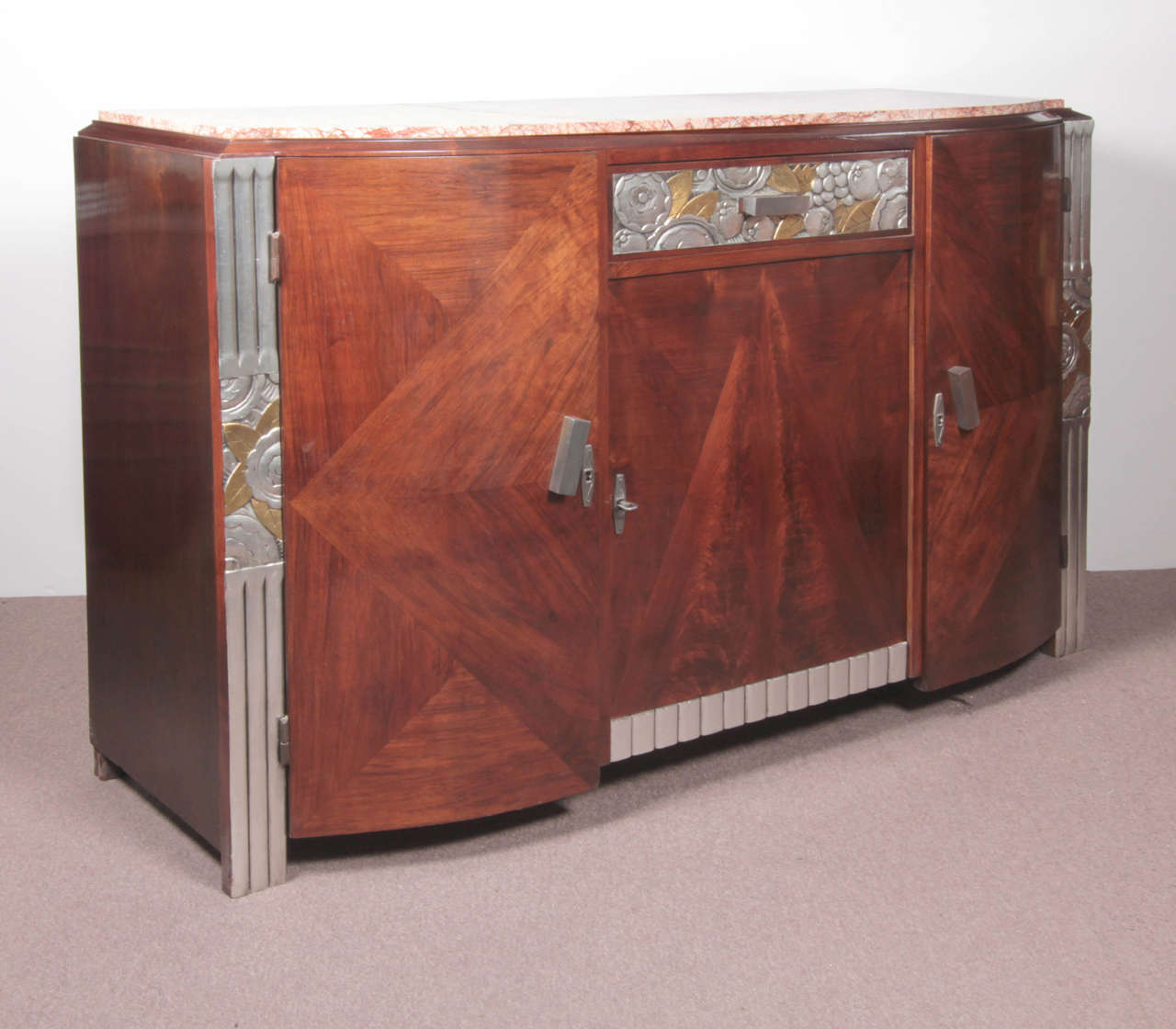 Original French Art Deco carved and inlaid three door cabinet. Beautifully crafted parquetry inlaid doors create a central pyramidal form amidst geometric shapes.
The top drawer features a hand carved gold and silver leaf frieze with stylized floral