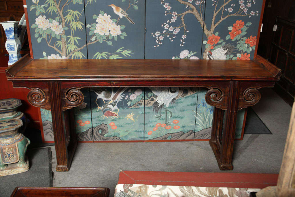 A carved elmwood Chinese console table from the mid-19th century with carved volutes and original brown-lacquer finish. This Chinese console table was hand-made with lacquered elm during the mid-19th century and retains its original finish. The