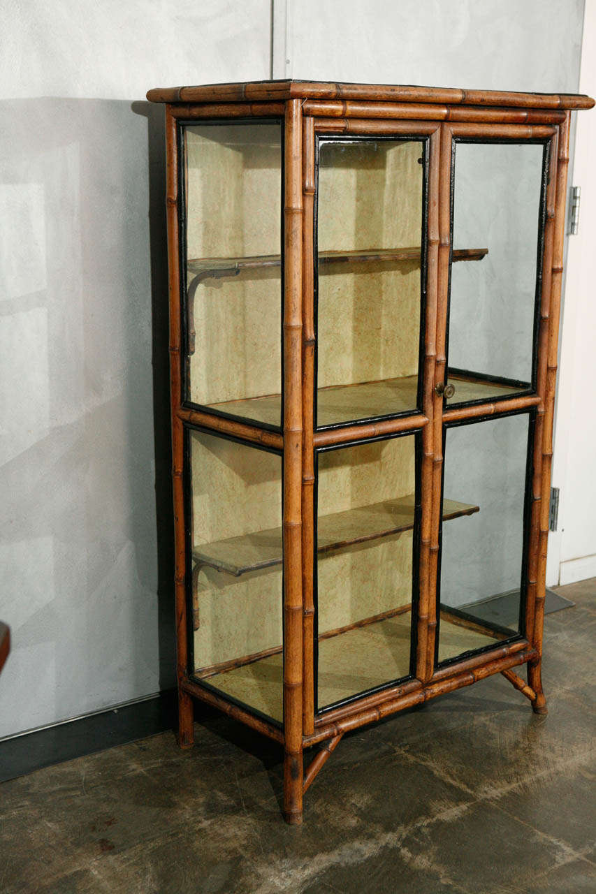 This delightful little bamboo cabinet is a beautiful 19th century piece with some really nice touches that make it suitable for a variety of settings.  The piece has hand painted black lacquer accents with green and gold lined shelves and walls. The