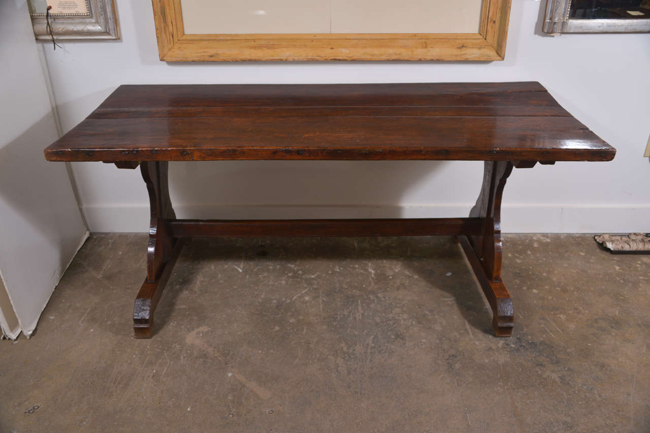 19th century French walnut monastery trestle table with a 1.75" thick top. The top is made of three planks of varying width. The two largest planks are on the outside and the smallest plank is in the middle. The plank widths are as follows: