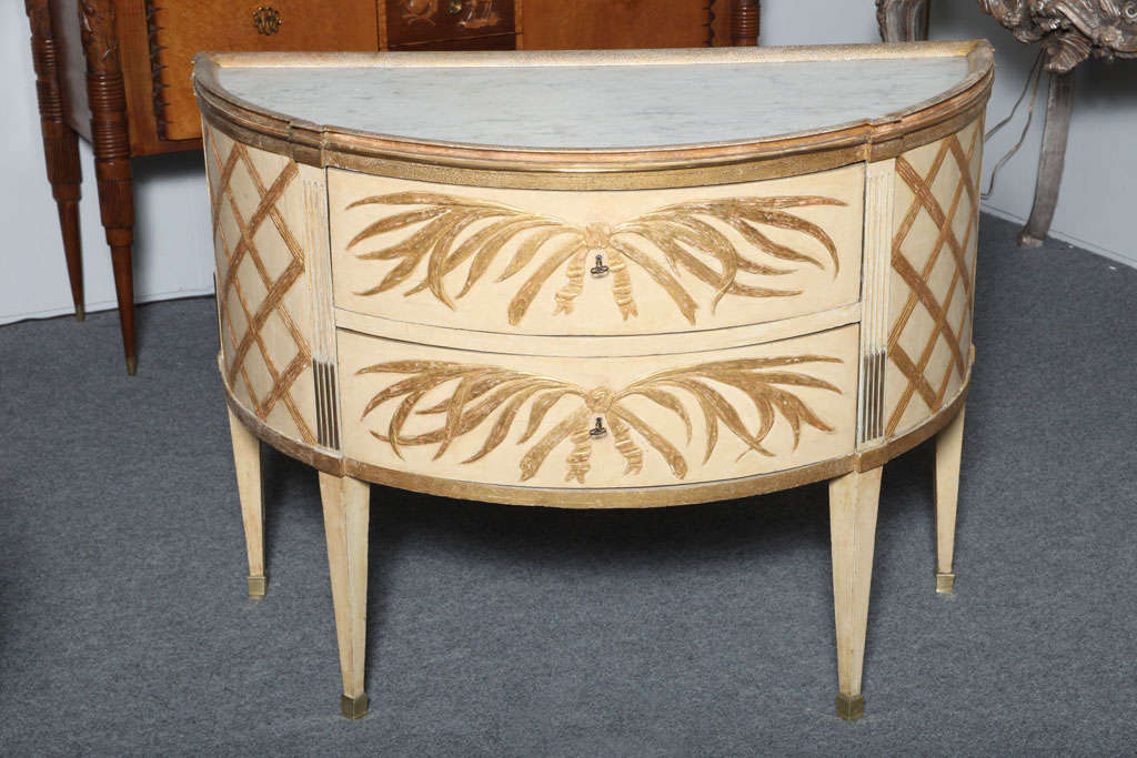 Unique pair of Baltic painted and gilt commodes, the demilune marble tops surmounted with gilt wood molded framed having a punched ground and cove molded underside, over two drawers with crossed palm branches tied with a ribbon, stop fluted upper