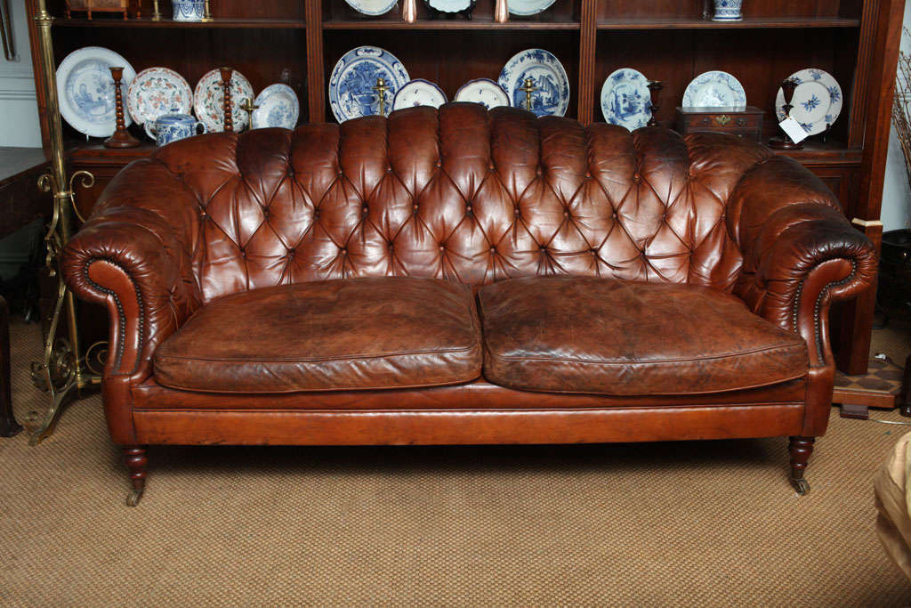 English Edwardian sofa in original leather upholstery, having rolled and tufted arms and back, two loose unbuttoned cushions, on turned legs with original brass casters, the whole with beautifully patinated tobacco leather upholstery.

