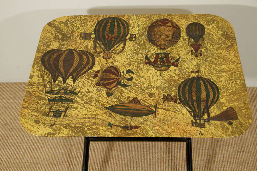 The rounded rectangular metal top, supported by black enamel base with gilt ball feet, the top applied with printed antique air balloons.