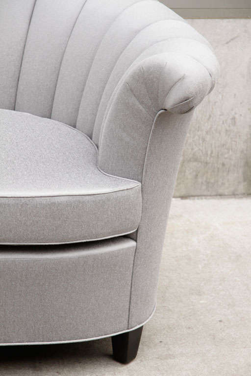 Hollywood channel-back upholstered sofa with concave apron, swept arms, and ebonized walnut feet.