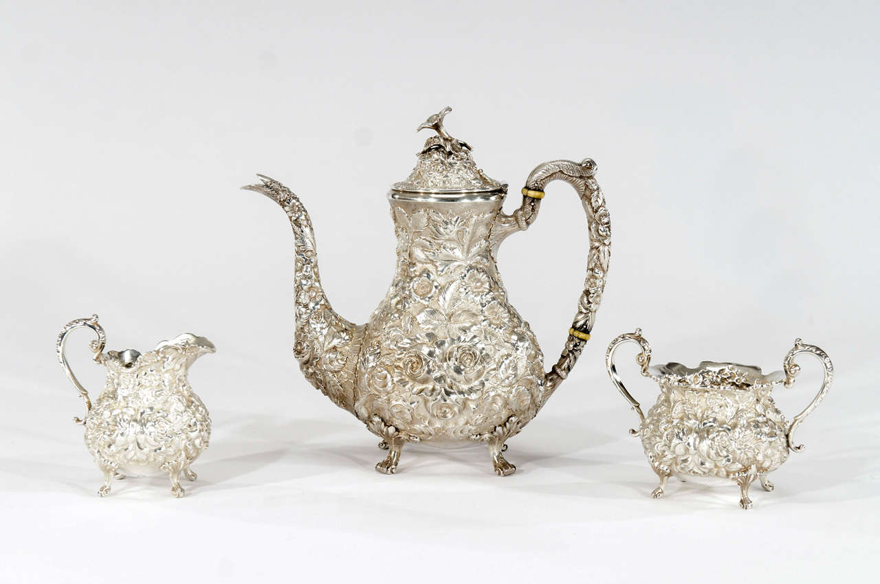 This gorgeous coffee service is made by Steiff in the Repousse pattern with all-over rose varieties encircling the body. The three matching pieces consist of a coffee pot, creamer and open sugar, all standing on four scrolled feet. The coffee pot