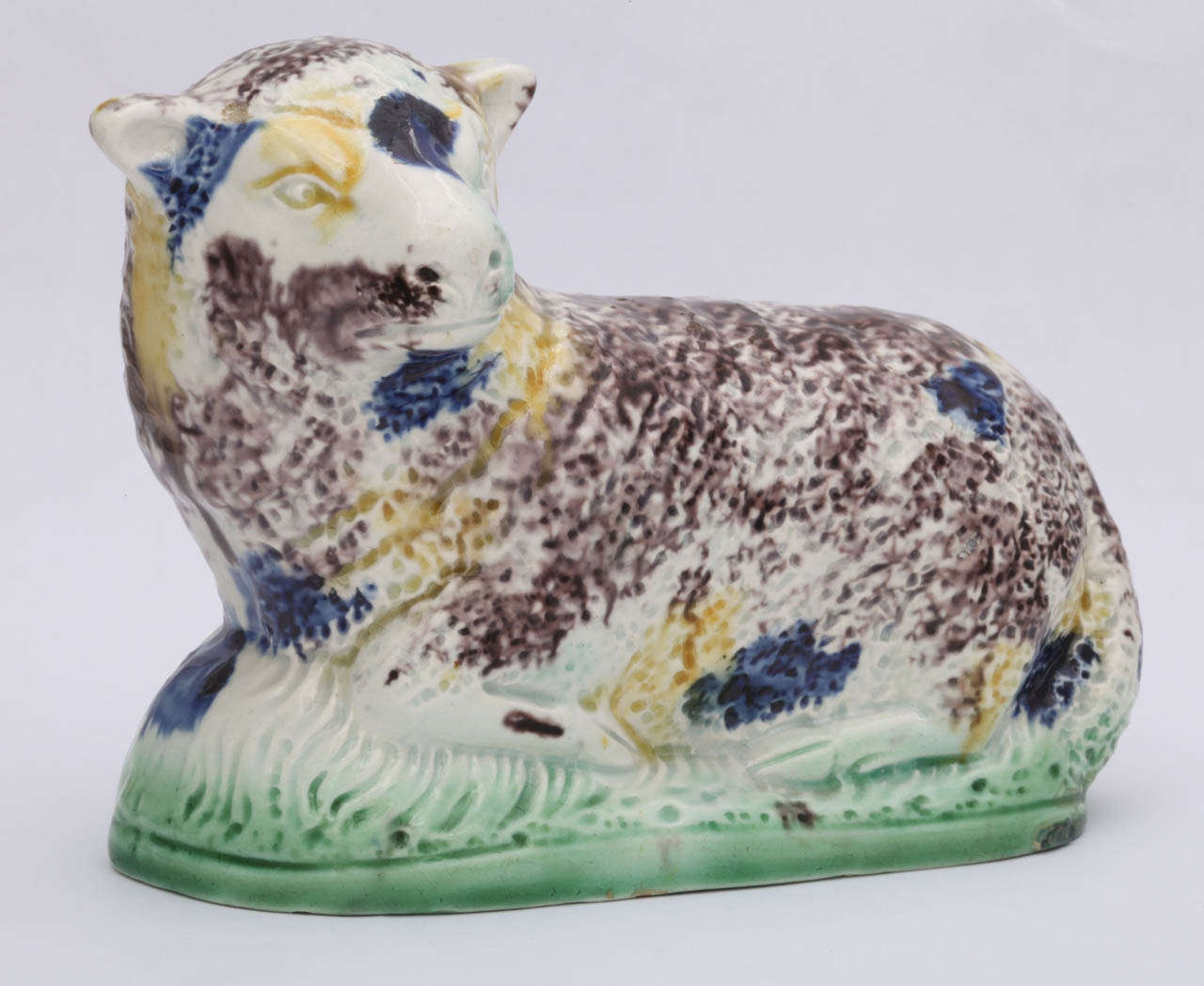 A fine English pearlware figure of a recumbent ewe decorated in underglaze Pratt colors.