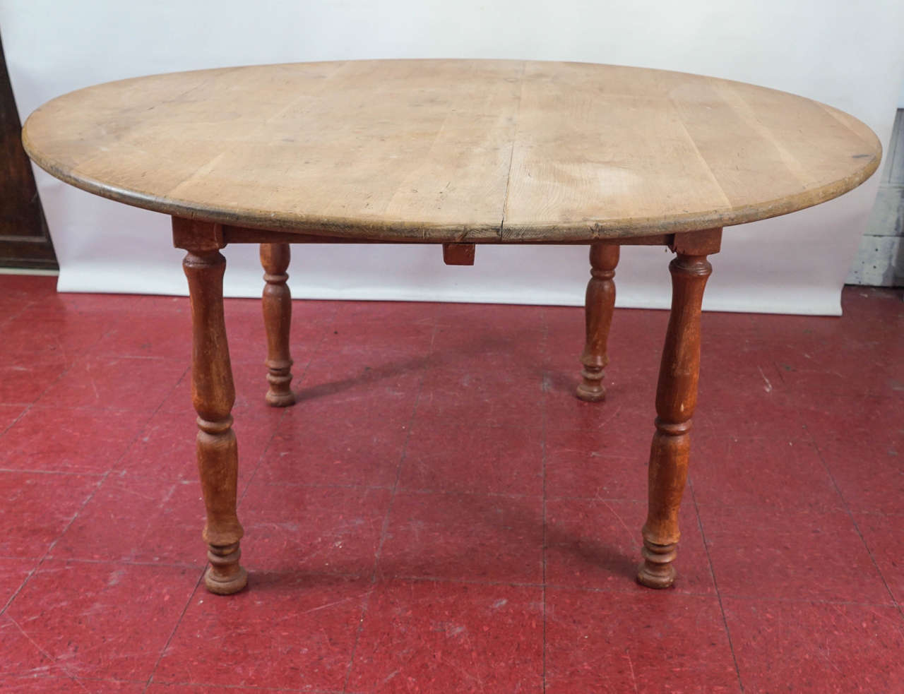 Round country farm dining table with a natural wood top and turned legs attached to a square base, this table will seat up to six or seven people. The base is painted red and has two permanent extensions that give added support to the