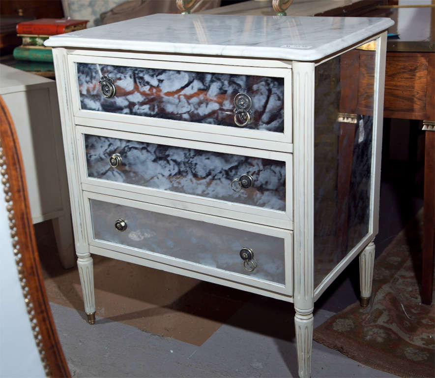 Painted French Directoire style commode, 20th century, white marble atop a conforming case fitted with three drawers, the drawers and the sides veneered with mylar, raised on fluted legs.