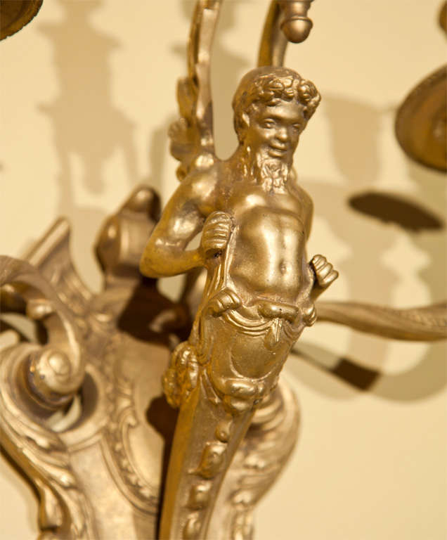 Pair of neoclassical style gilt-metal wall sconces, 20th century, each has three arms, centered by a figurine.