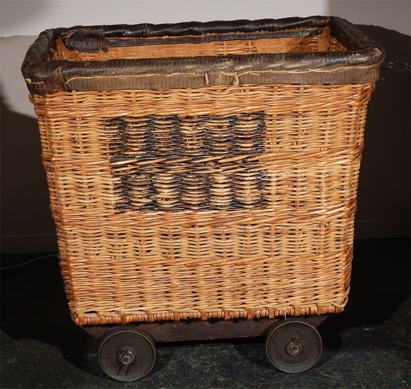 This vintage French hotel laundry cart is a great functional and decorative item. It is very solid, and well made. The rattan is thick, the leather top lip is heavy and padded, the iron wheels are big and roll easily, the inside has a thick canvas