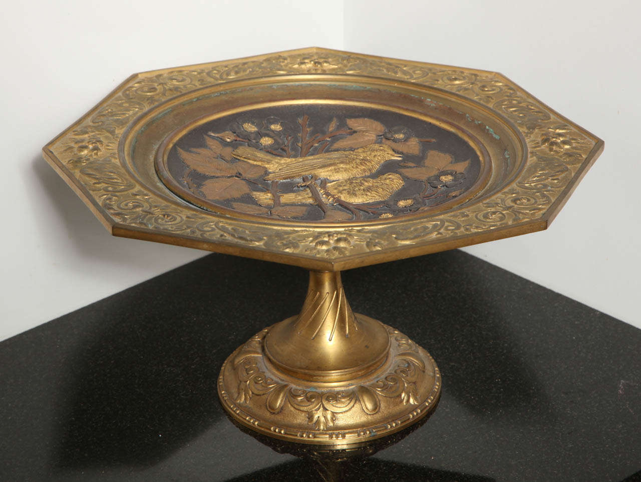 This unique plate in bronze and brass with birds and floral embossed makes this antique superb. It has an octagon shape plate at the top and circular bottom base. The embossed birds are highlighted by the floral design and its dark background.
The