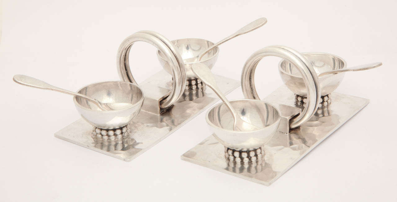 Beautifully designed by Jean Despres (1889-1980), this set of four silver plated salt cellars bears his trademark hammered finish and silver bead detailing.  Center ring serves as a handle for ease in carrying.  Each cellar has it's own spoon.