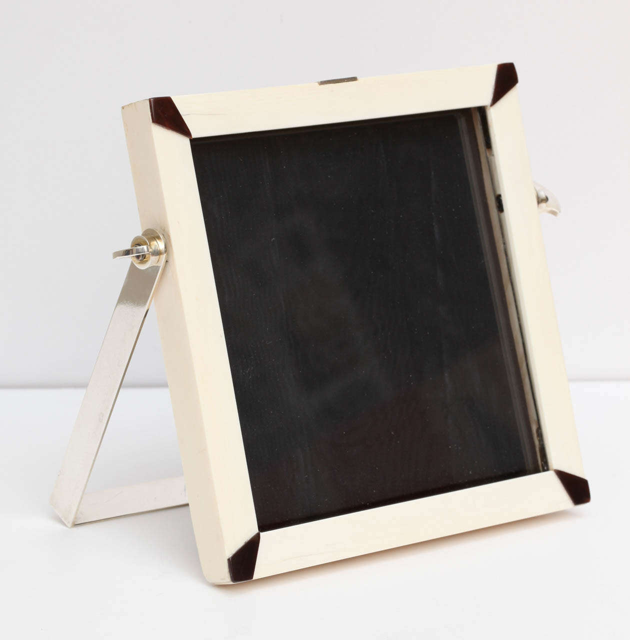 An ivory frame with tortoiseshell details inlaid on each corner. A beautifully constructed piece made with a sterling silver articulated easel. Even the nuts and screws holding the easel are marked sterling. The square shape is  quite interesting