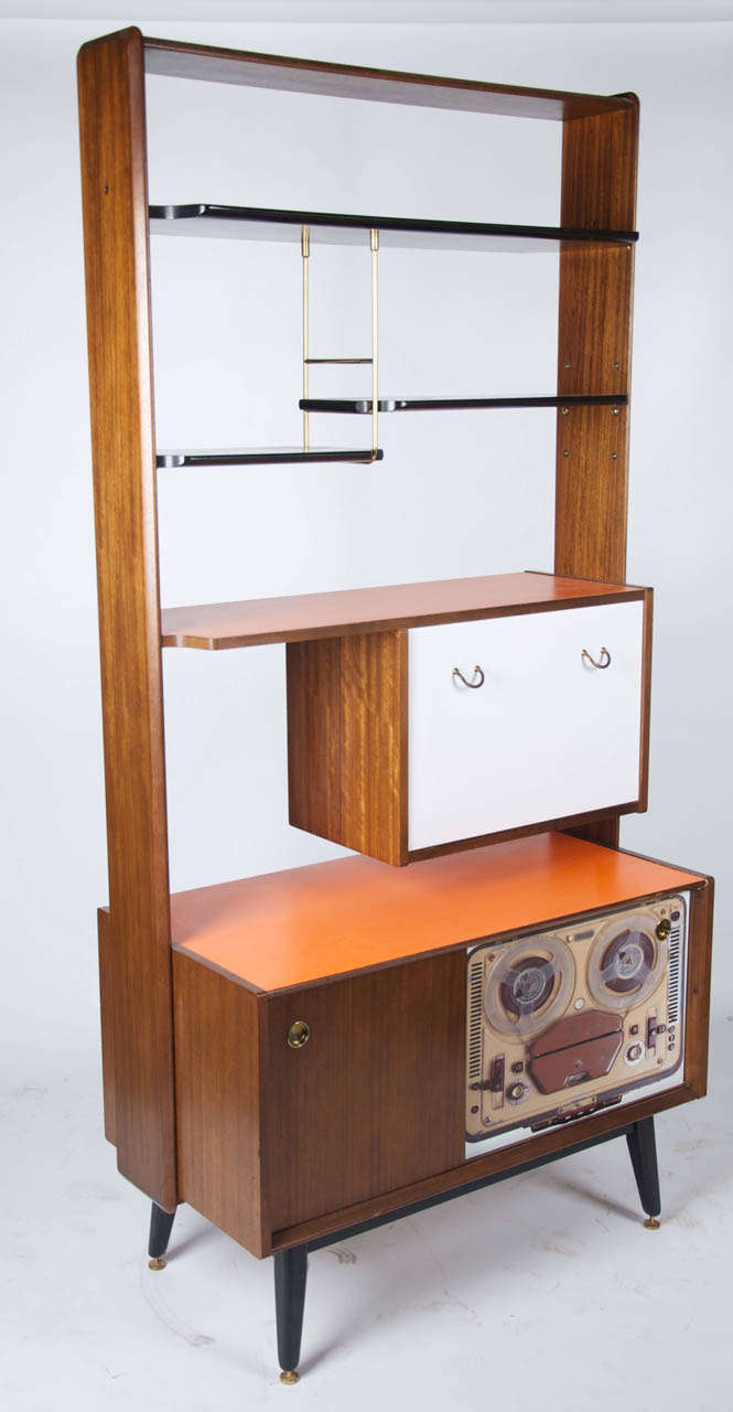 A British 1960's teak and ebonised wall unit with graphic and plain veneer surfaces. The lower sliding door having a laminate veneer image of a reel to reel tape recorder.