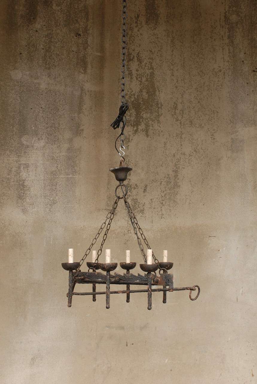 A French wrought iron six-light chandelier composted of antique elements. This French chandelier features a central spit jack to which are attached six twisted torchères. Four sets of links join the body part to the old canopy. This chandelier has