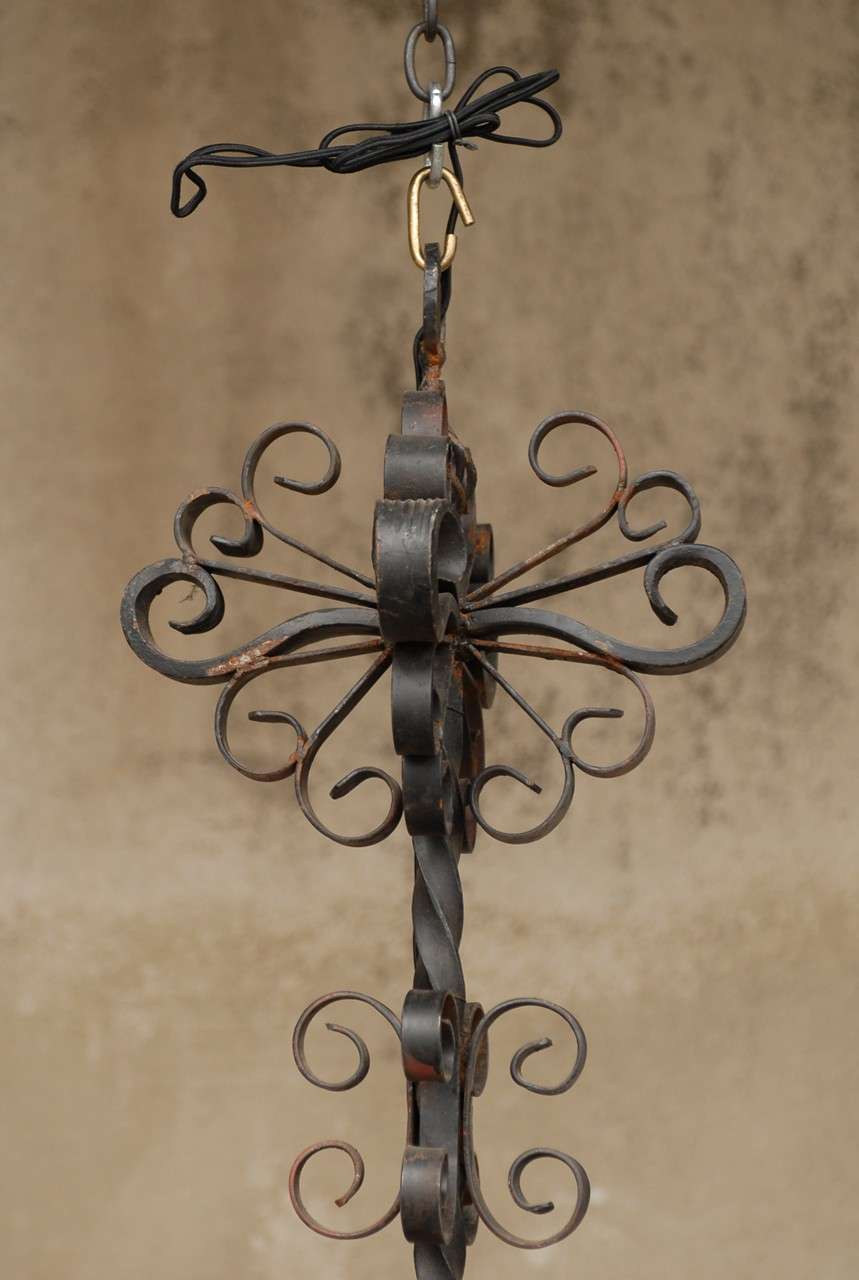 A French forged iron four-light chandelier. This French vintage forged iron chandelier features a compound of curls in its top part, intertwined around a twisted central column. Its lower part is decorated with a twisted pierced finial. This