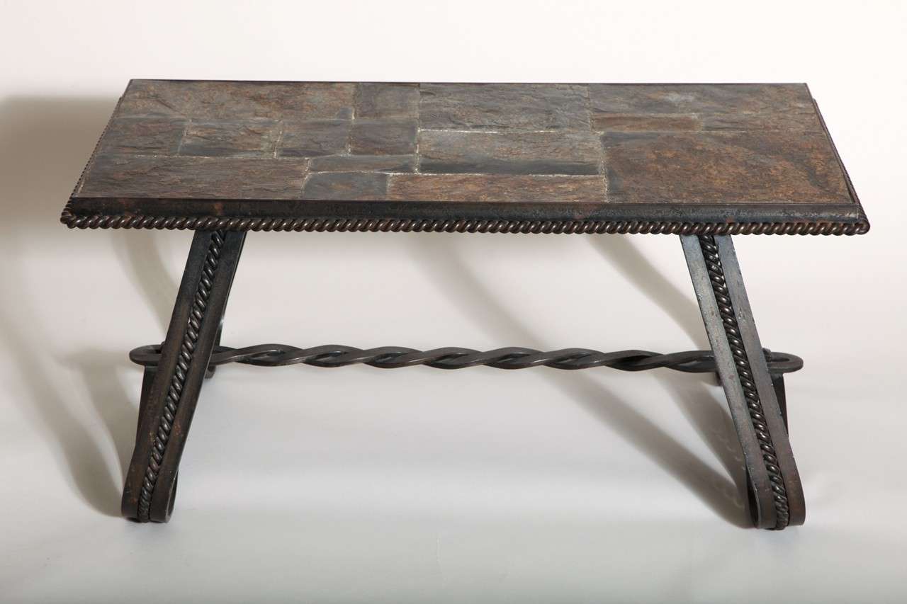 This table has a top of multiple rectangular pieces of slate bordered by a wrought iron twisted rope atop two continuously curved wrought iron legs with rope decoration down centre and connected by twisted wrought iron stretcher.