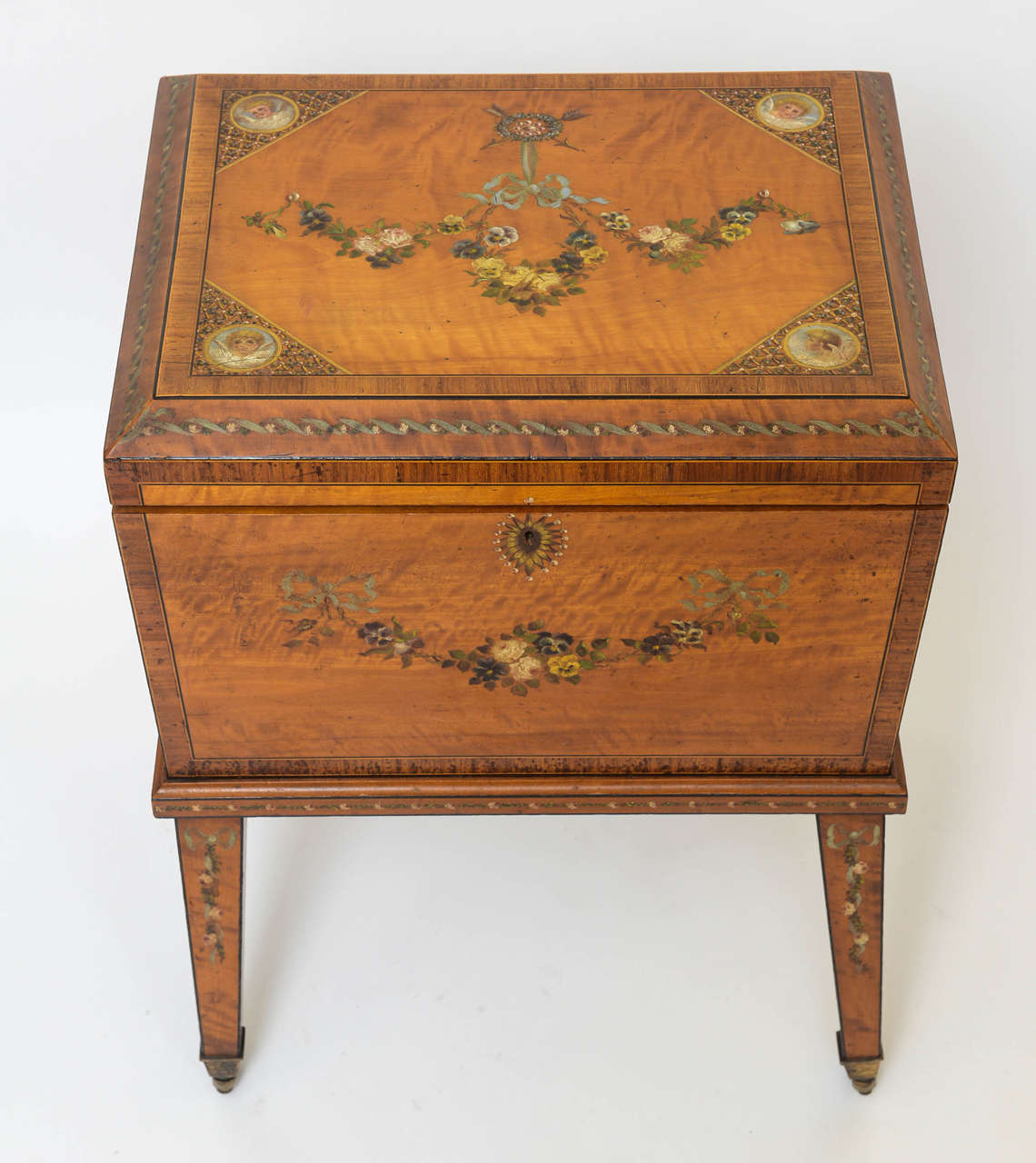 Adam style wine cooler with hand-painted decorations, adorned with cherubs and floral festoons. Satinwood. Now felt lined and raised upon original brass castors.