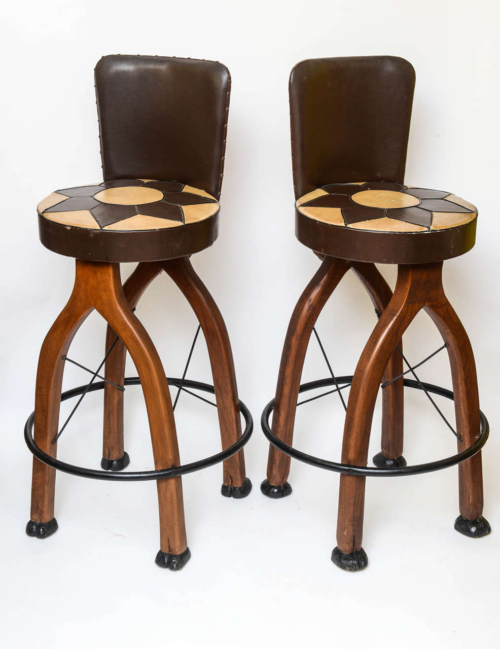 Outstanding fanciful bar stools with camel motif wood carvings head, neck and feet. The stools appointed with iron footrests. The leather like seat covers are original (worn).