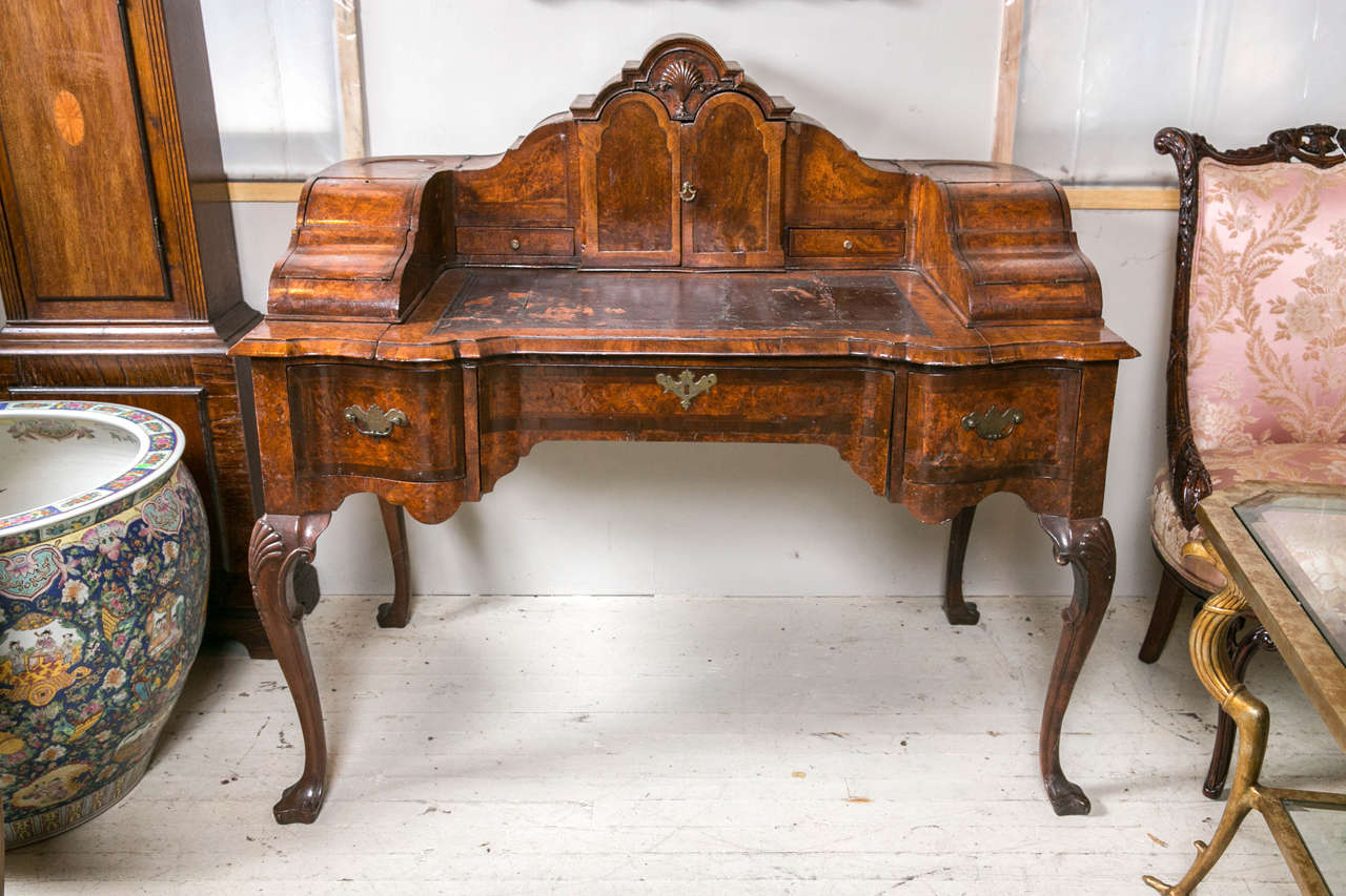 This desk,  circa 1800, is of burl walnut  veneers and walnut solids.  It is very much in the form of an English Carlton House desk. The arched top has a central cabinet,  2 small drawers flanking and  2 lidded, hinged compartments on either end. 