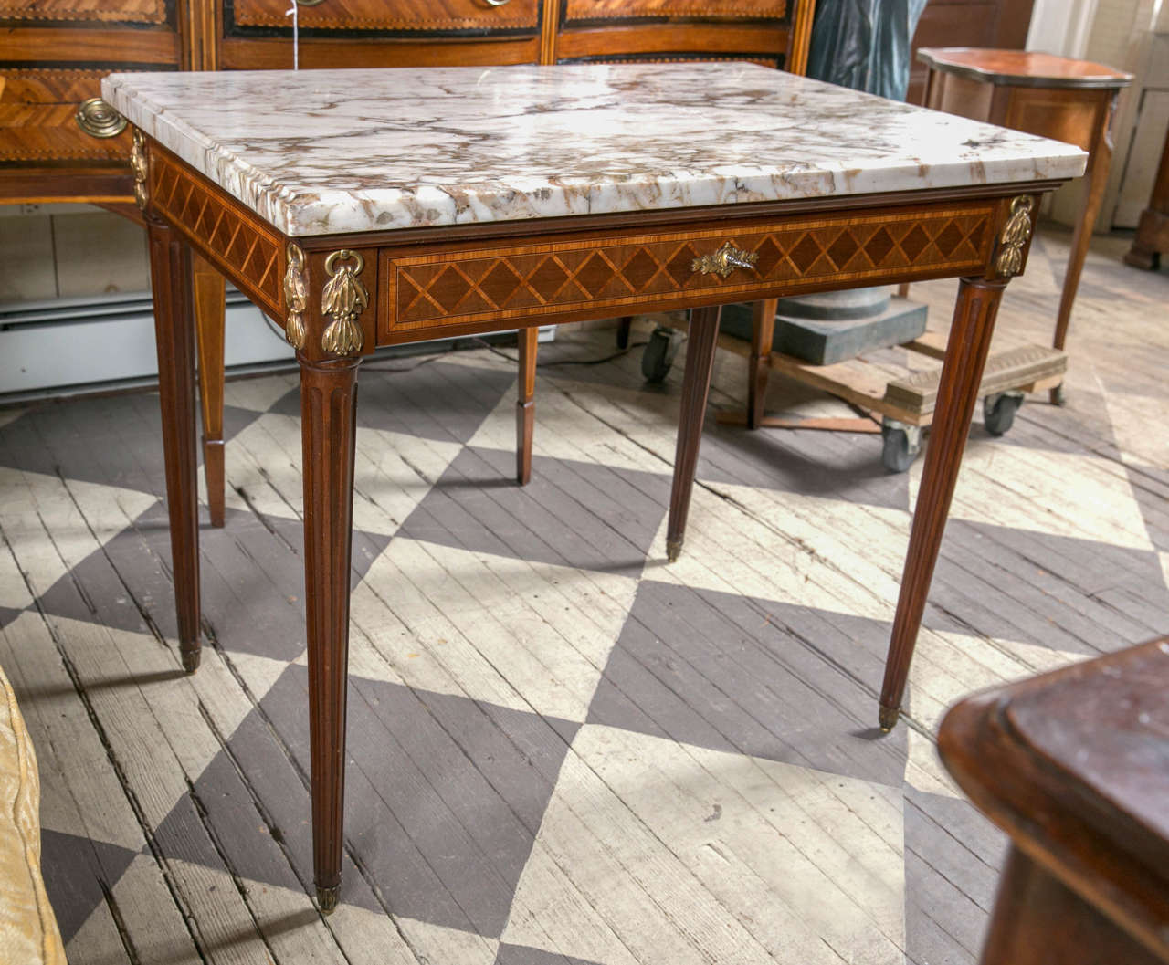Cove edge marble over a marquetry in laid base, with one drawer. Marquetry of what appears to be mahogany, sycamore and satinwood. Gilt bronze mounts at each corner and escutcheon. Gilt bronze capped feet. Fluted legs.