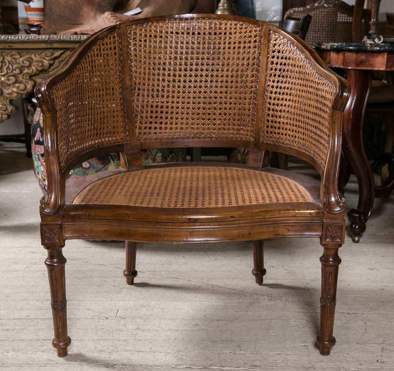 This chair in the bergere manor has caned seat, back and sides. The back rail forms the contiguous arms which gently curve to the seat rail. The front of the seat rail is a slight serpentine form. The back and sides are rounded. Raised on tapered