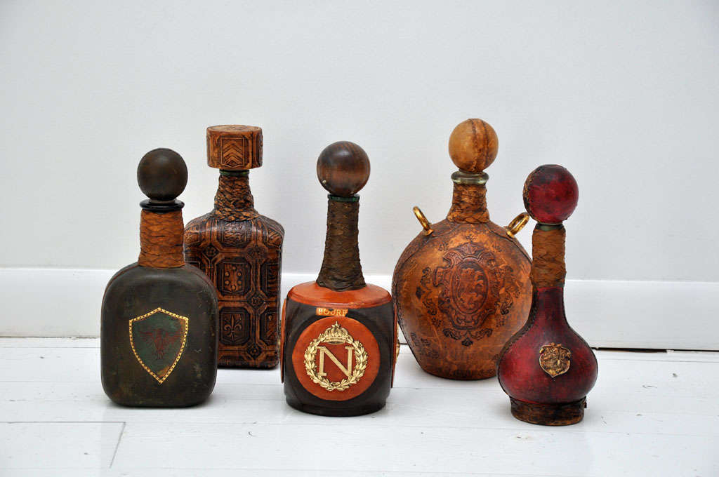 Collection of English leather wrapped decanters with metal emblems.  Decanters range in size from 4