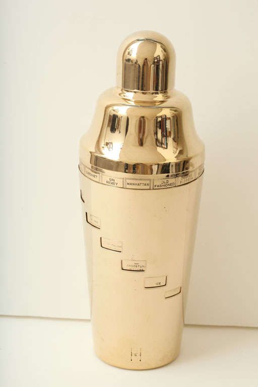 A Napier ‘recipe’ cocktail shaker in the original rare gold-plated finish. The outer sleeve rotates to reveal recipes for 15 different cocktails that can be made by reading the instructions through the cut openings on the outer sleeve. The cap