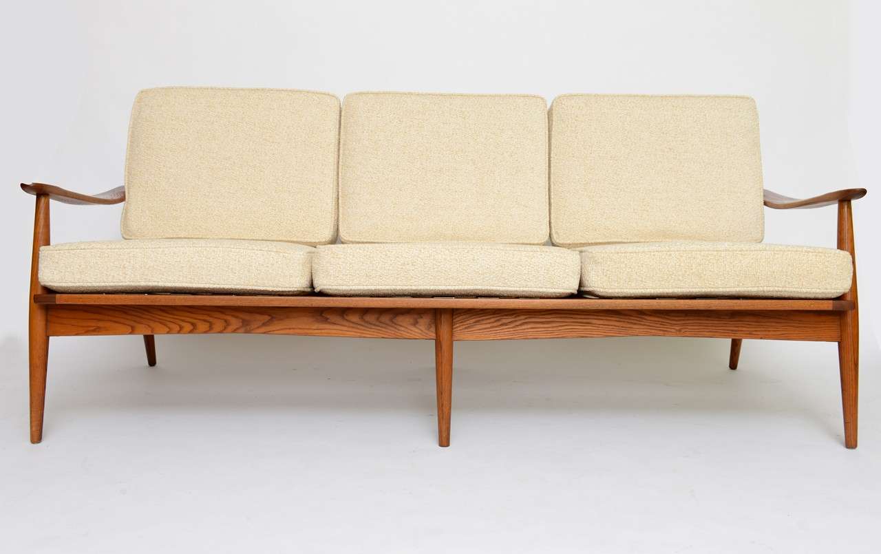 SOLD  Beautifully tapered legs and shaped wide oak arms highlight this Danish three seat sofa.  With lathe turned teak and shaped oak arms, it has a spindle back design and a wonderful profile all around.  New cushions upholstered in a creamy