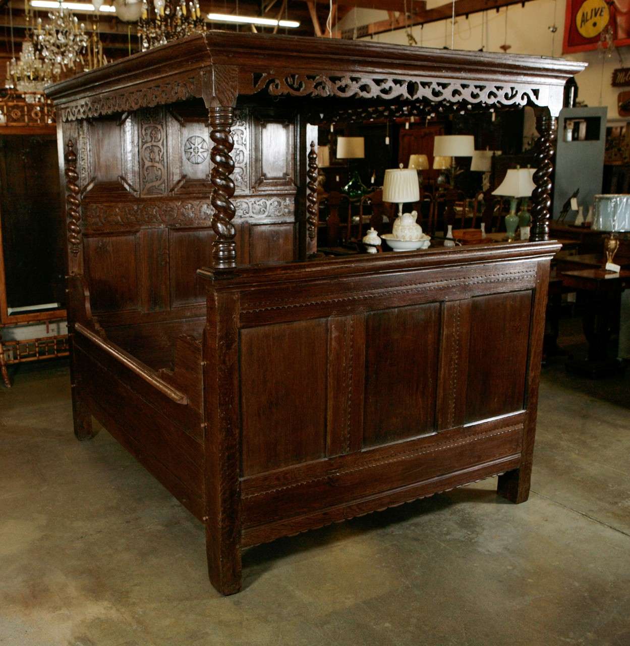An antique oak tester bed with a molded and pierced carved cornice, a carved frieze and a geometrically fully paneled roof supported by twist half columns extending from the three paneled foot board. The supporting head board has six panels and chip