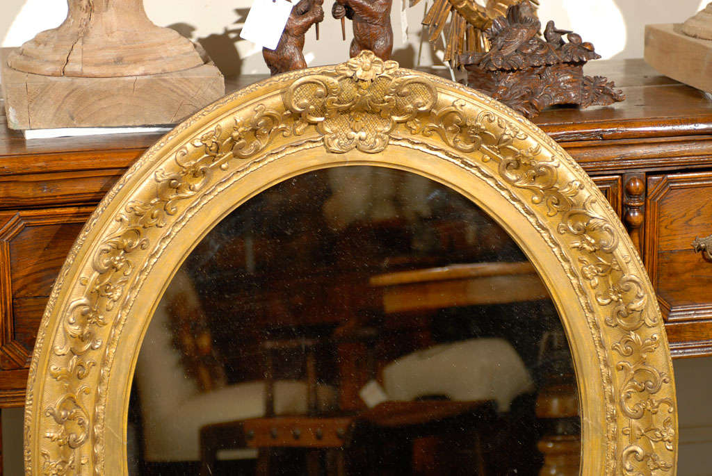 An English mid to late 19th century mirror with a giltwood oval frame with a molded convex outer border ending if a flat plain inner border. The oval mirror plate is set within a slightly crested molded frame finely carved with intertwining and