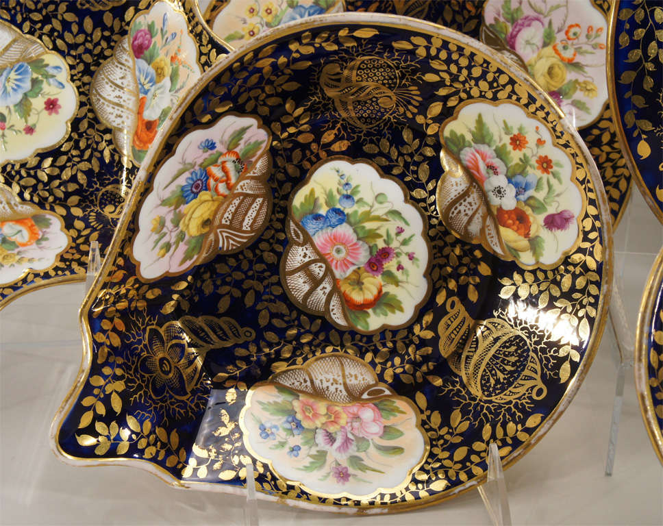 An extraordinary, museum quality botanical and mollusk decorated dessert service. Each uniquely decorated piece is hand painted with all different shells and flowers on a cobalt blue ground, all highlighted in gold. There are 12 dessert plates, 2