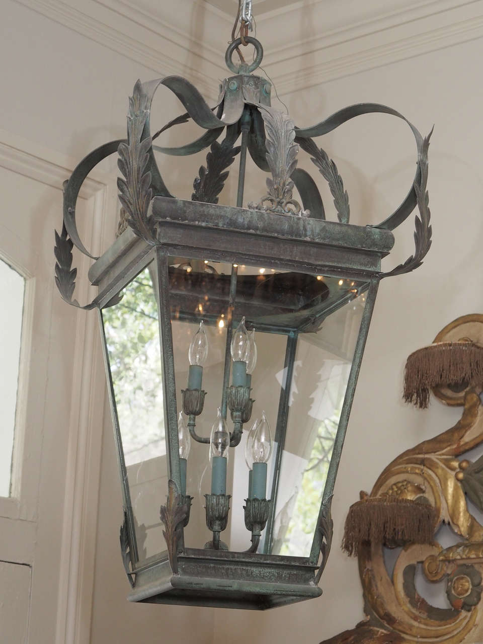 A large, verdigris colored lantern topped with acanthus leaves which form a simple, open crown.