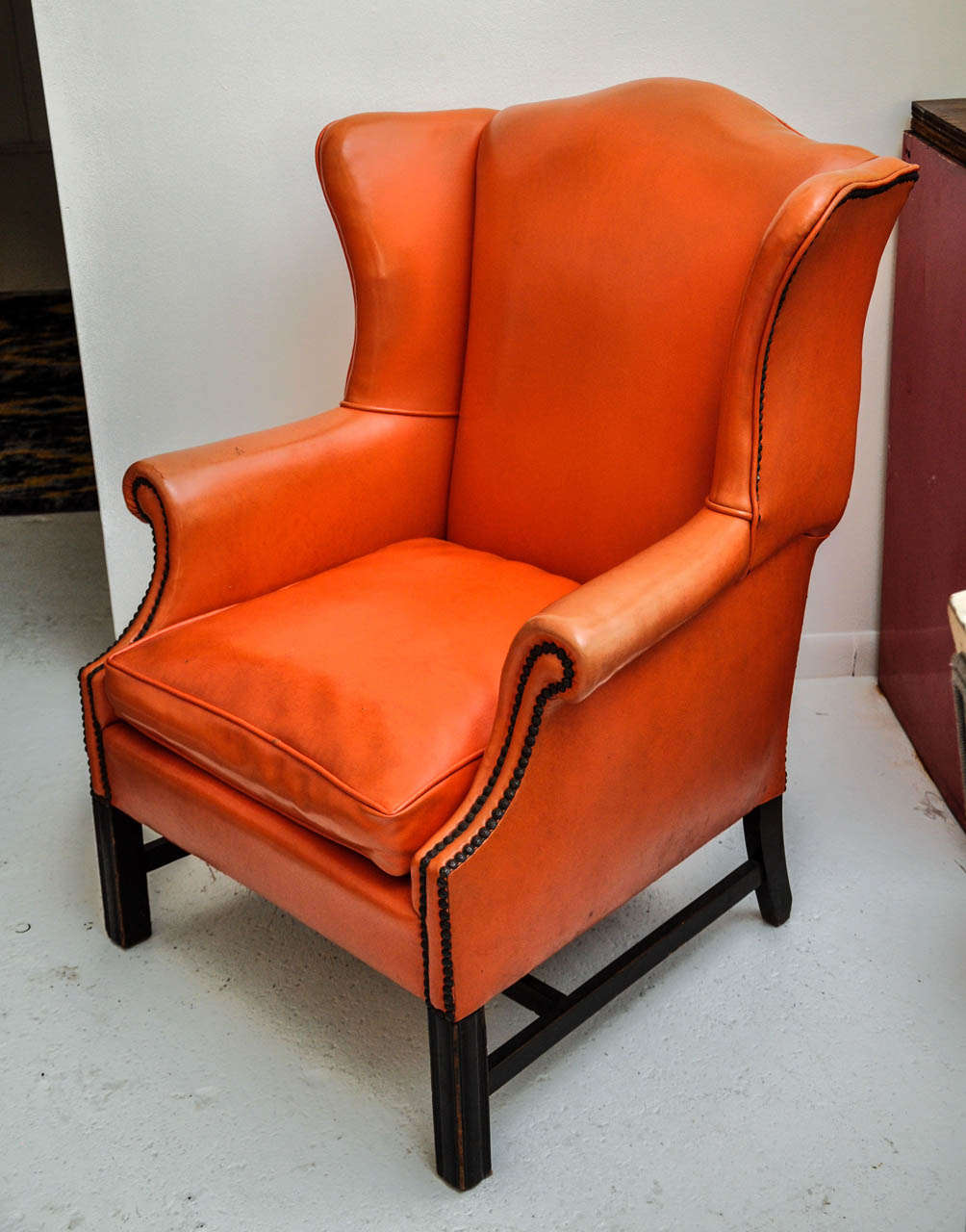 Vintage Orange Leather Wing Chair with distressed espresso wood base and antique brass nailhead trim
