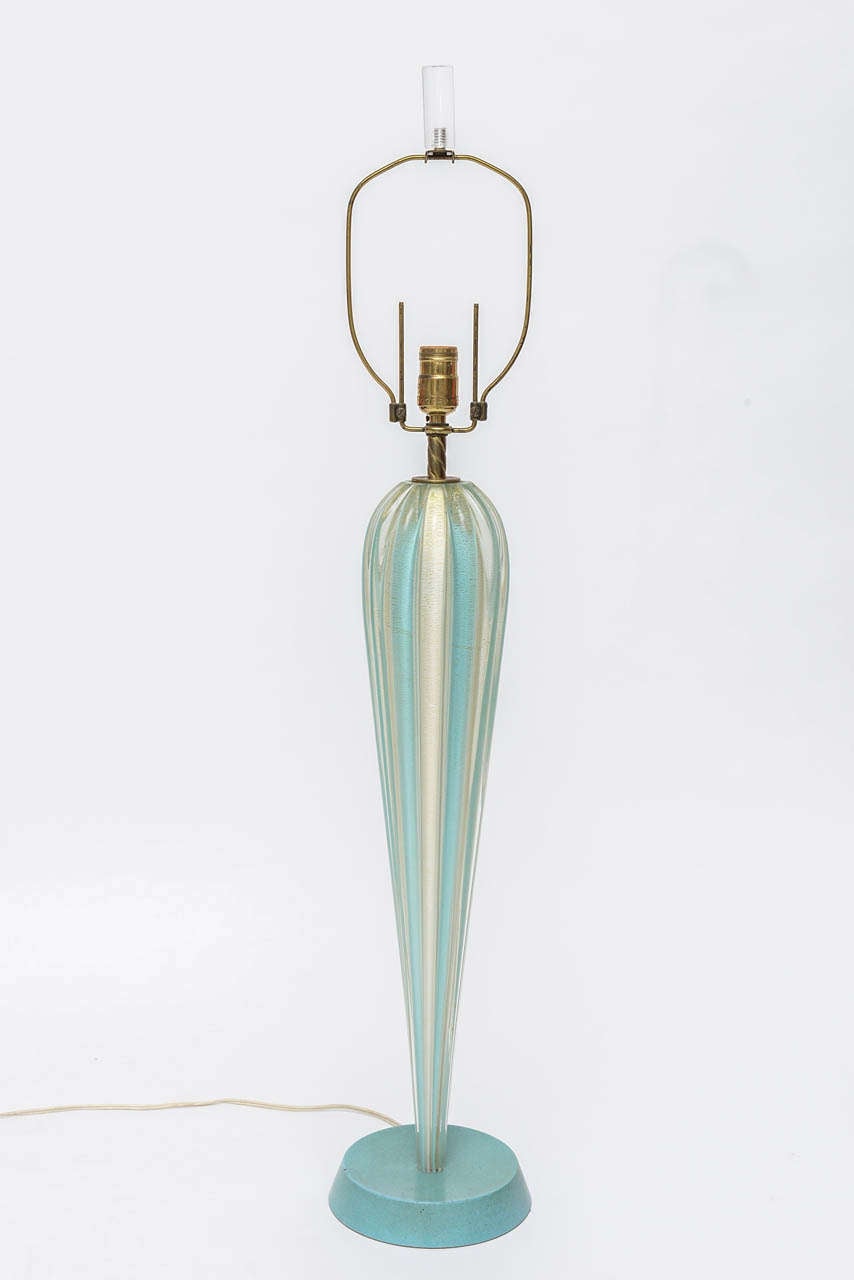 Single light blue and white murano glass lamp with golden flecks throughout, featuring a twisted brass neck and hardware, lucite finial top, and matching blue metal base.