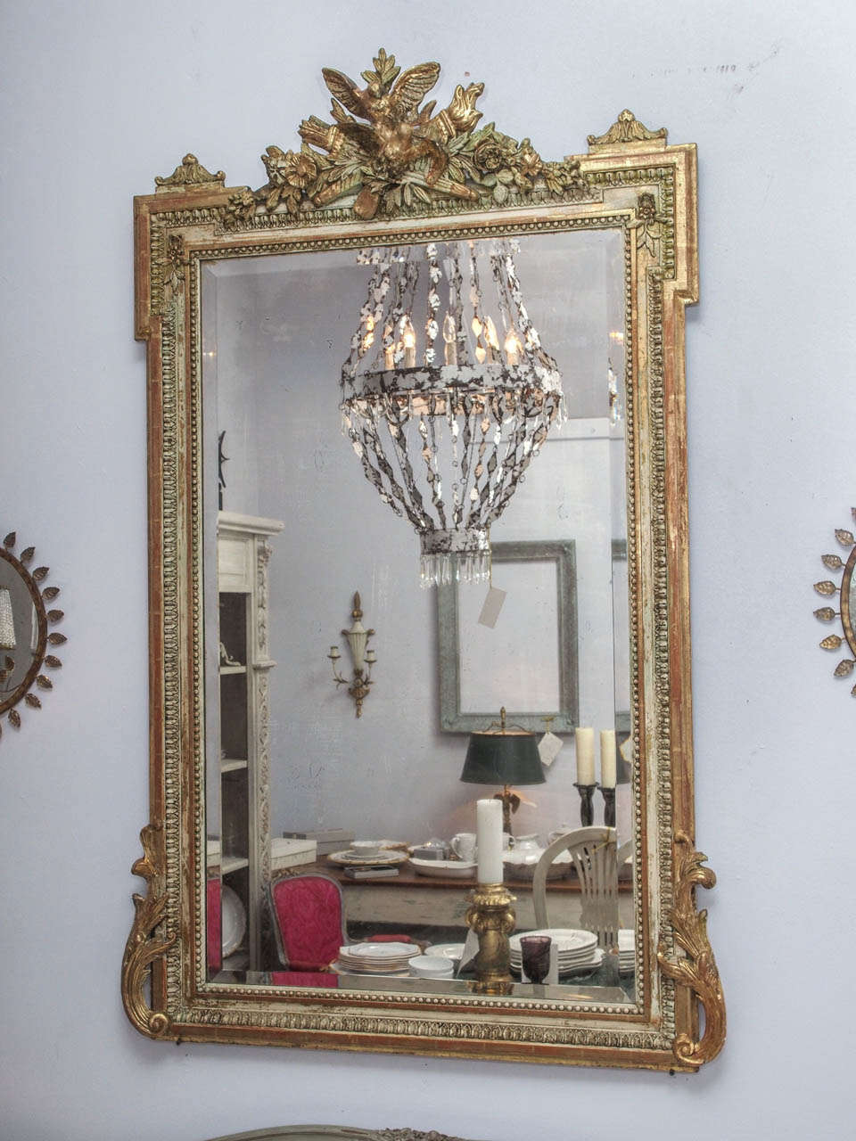 Handsome French C1890 richly carved wood, gesso, paint, and gilt mirror with Neo-classical details in the Louis XVI style. A beaded edge borders the beveled mirror, which is housed in a frame surmounted with a quiver,torch, bird and floral motif.