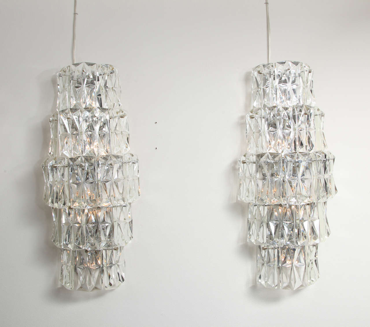 A pair of contemporary design oversized crystal sconces with five tiers of large rectangular faceted drops concealing electric light sockets.