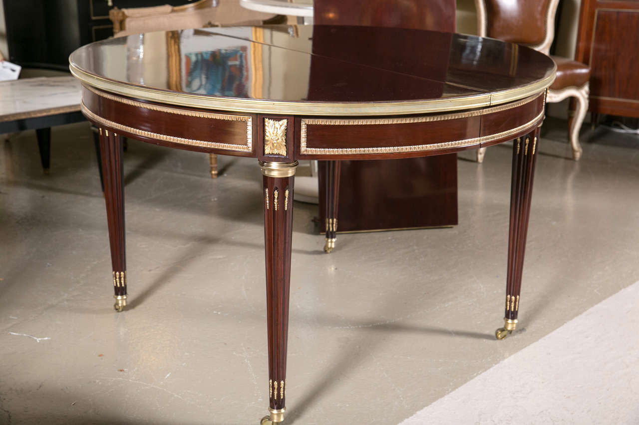 Spectacular two-leaf circular French dining table by Maison Jansen. This is quite simply the finest of tables with F. Linke quality bronze mounts. The Louis XVI style legs having bronze casters and sabots with lower and upper flamed bronze mounts