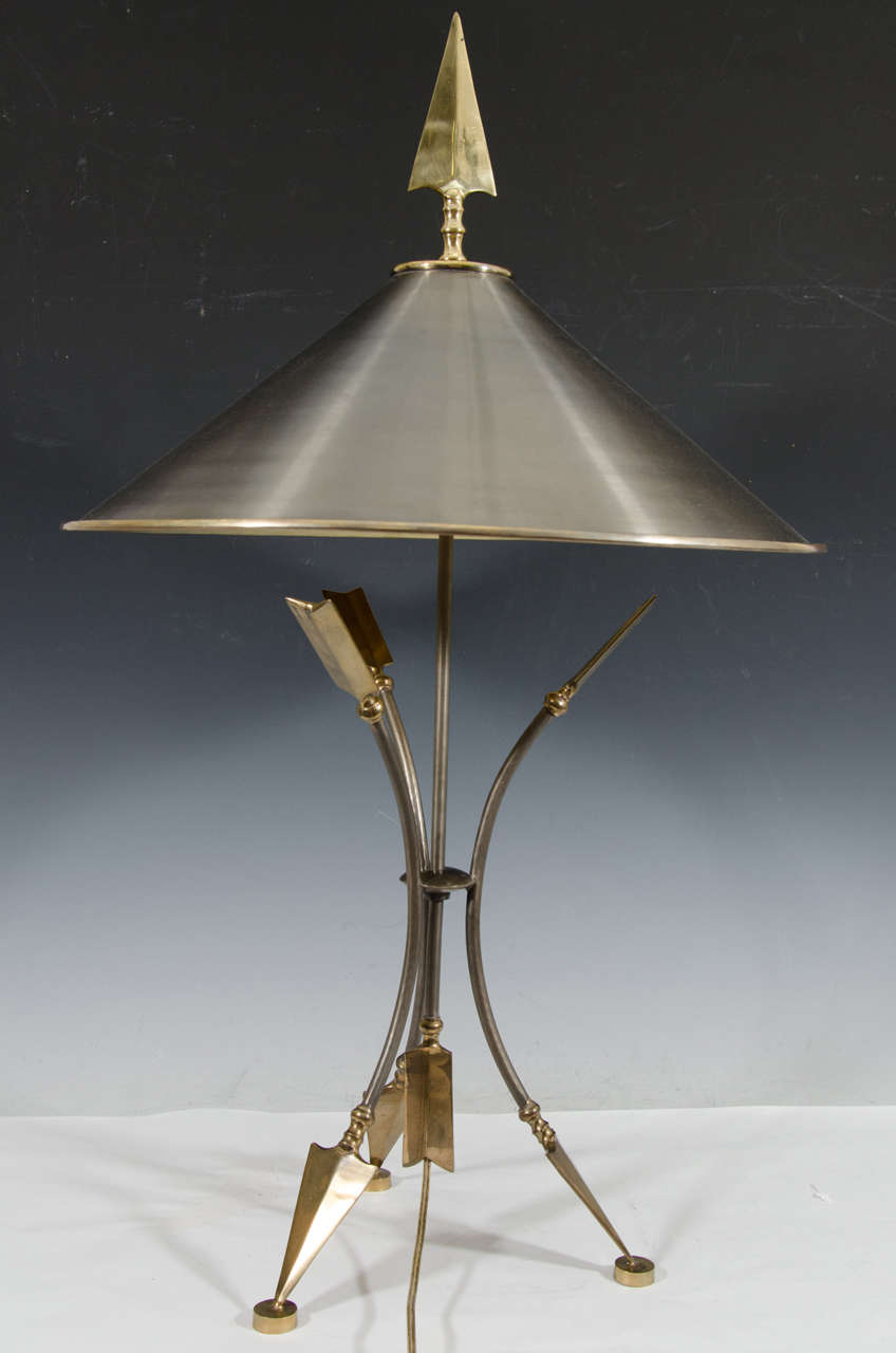 A 20th century pair of stylized brass and silvered metal arrow table lamps with conical shades and tripod bases. Good vintage condition with age appropriate wear and patina. Some loss of silver finish.