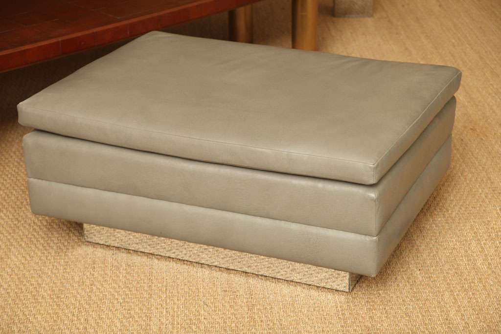 This period ottoman features a floating chrome wrapped base and original Edelman leather upholstery. The leather is a soft gray and features an attached cushion top.