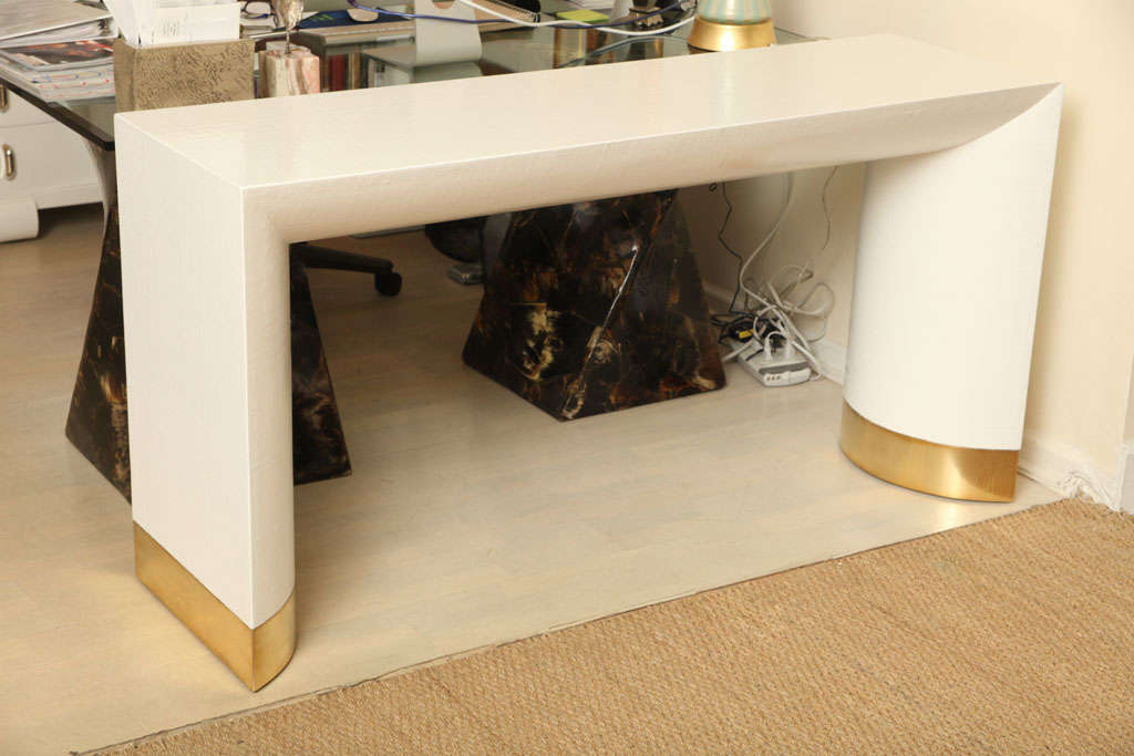 This sensational console table is simplistic yet modern. This piece features two curved legs with polished brass bands. It has been newly re-lacqered to bring out the sought after linen texture of the time period.