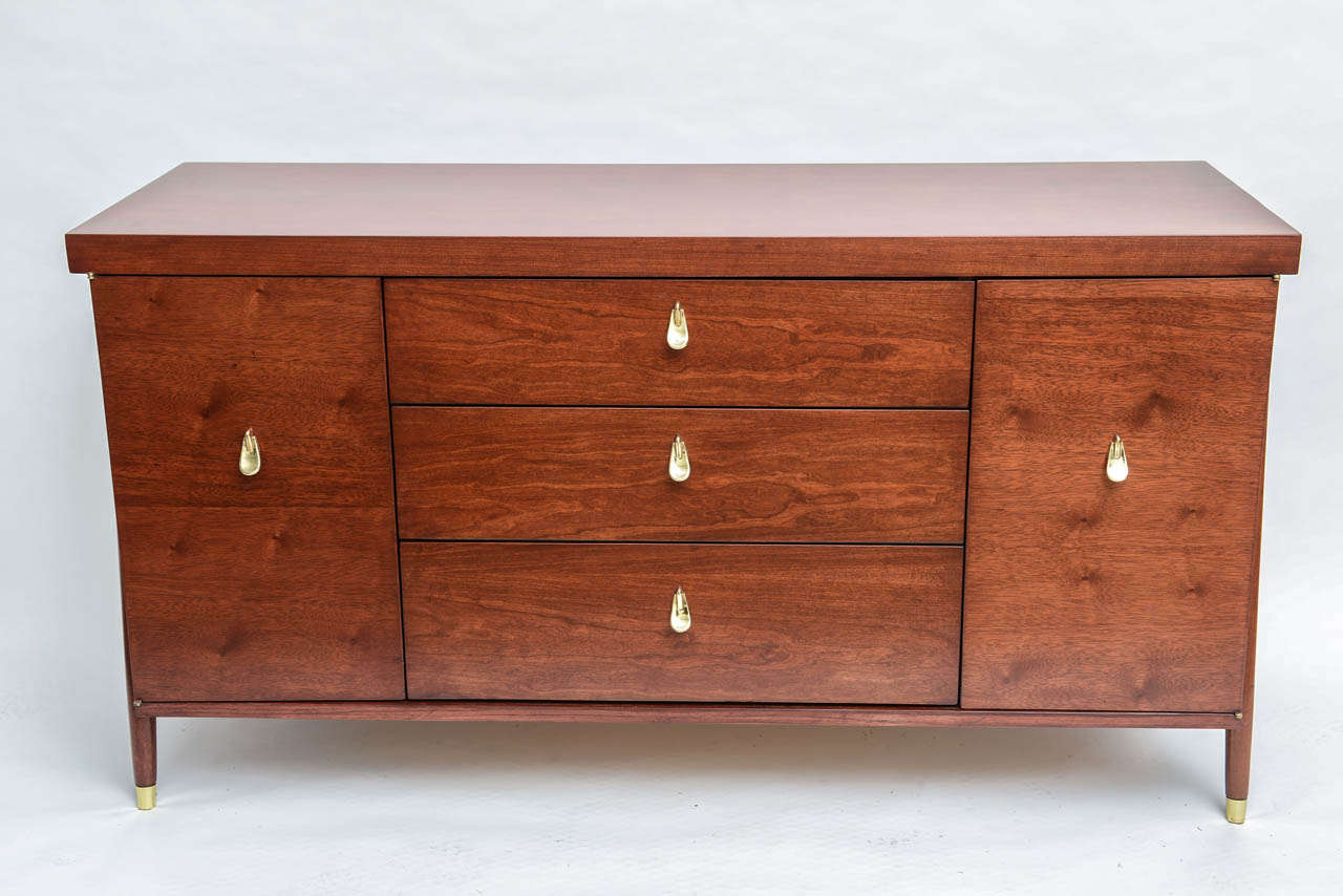 Beautifully finished Italian mahogany credenza with original brass pulls and sabots; featuring three doors flanked by two doors revealing shelves. The color and feel of the wood in conjunction with the mid century design & brass pulls turns this
