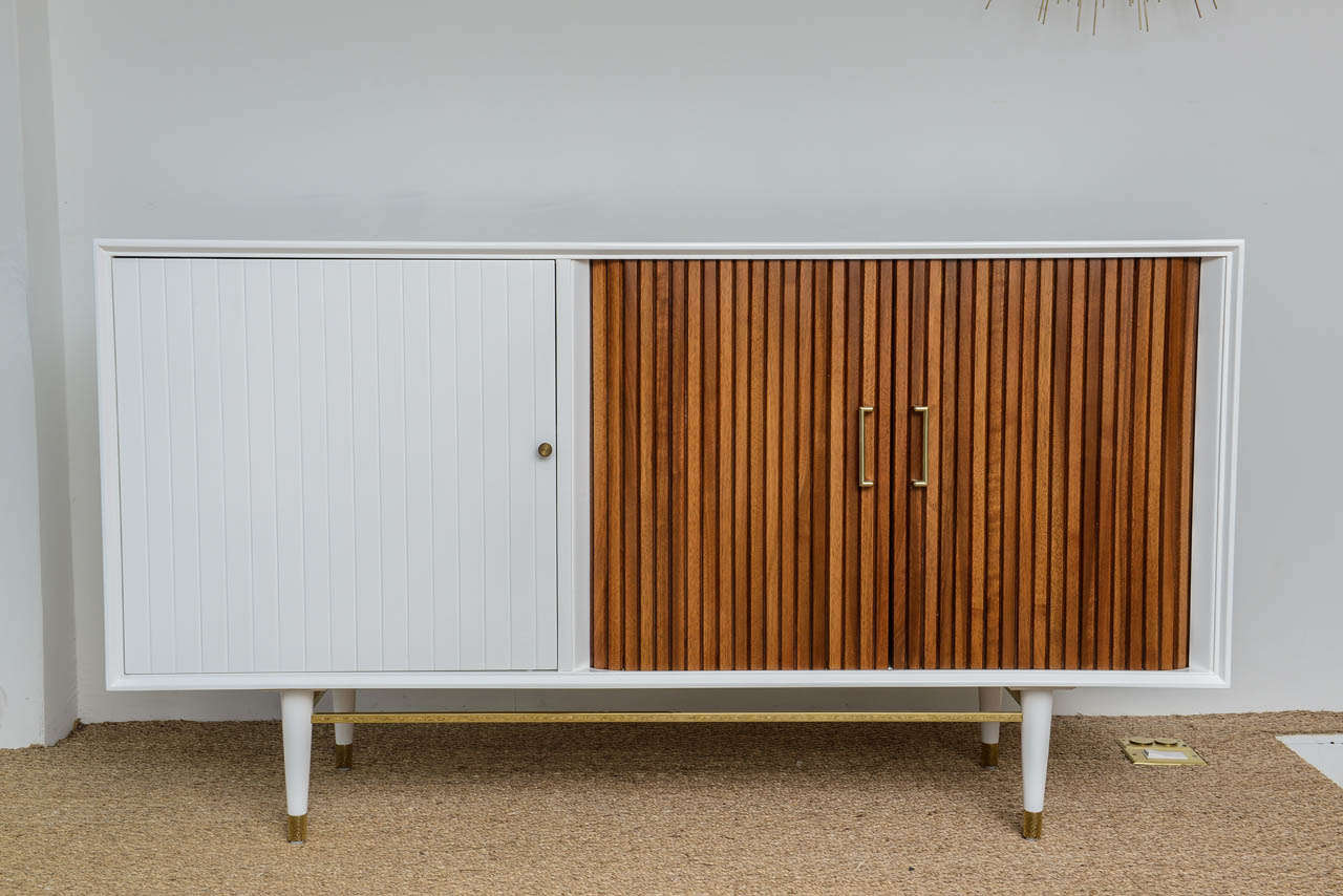 Pair of credenzas in high gloss white lacquer with newly finished walnut tambour doors revealing lower and middle shelves. Excellent storage capacity with a wide door adjacent to the tambour doors. The beautiful brass stretchers, sabots, and pulls