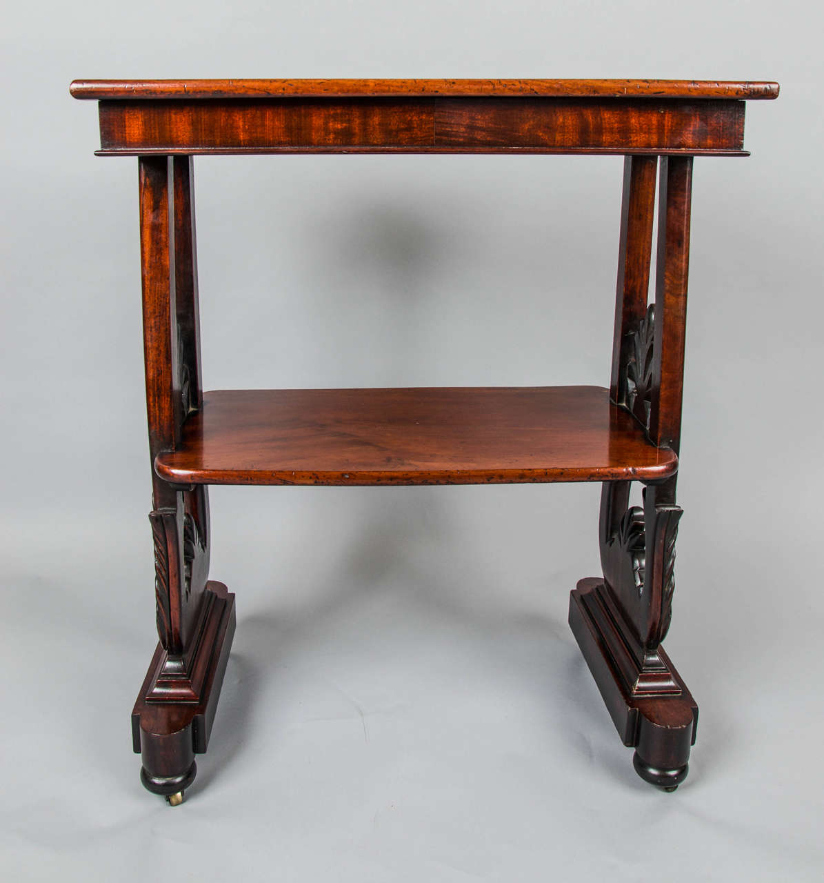 An early Victorian mahogany side or occasional table with a lower tier and exquisite carving to the sides, in the form of anthemion leaves.