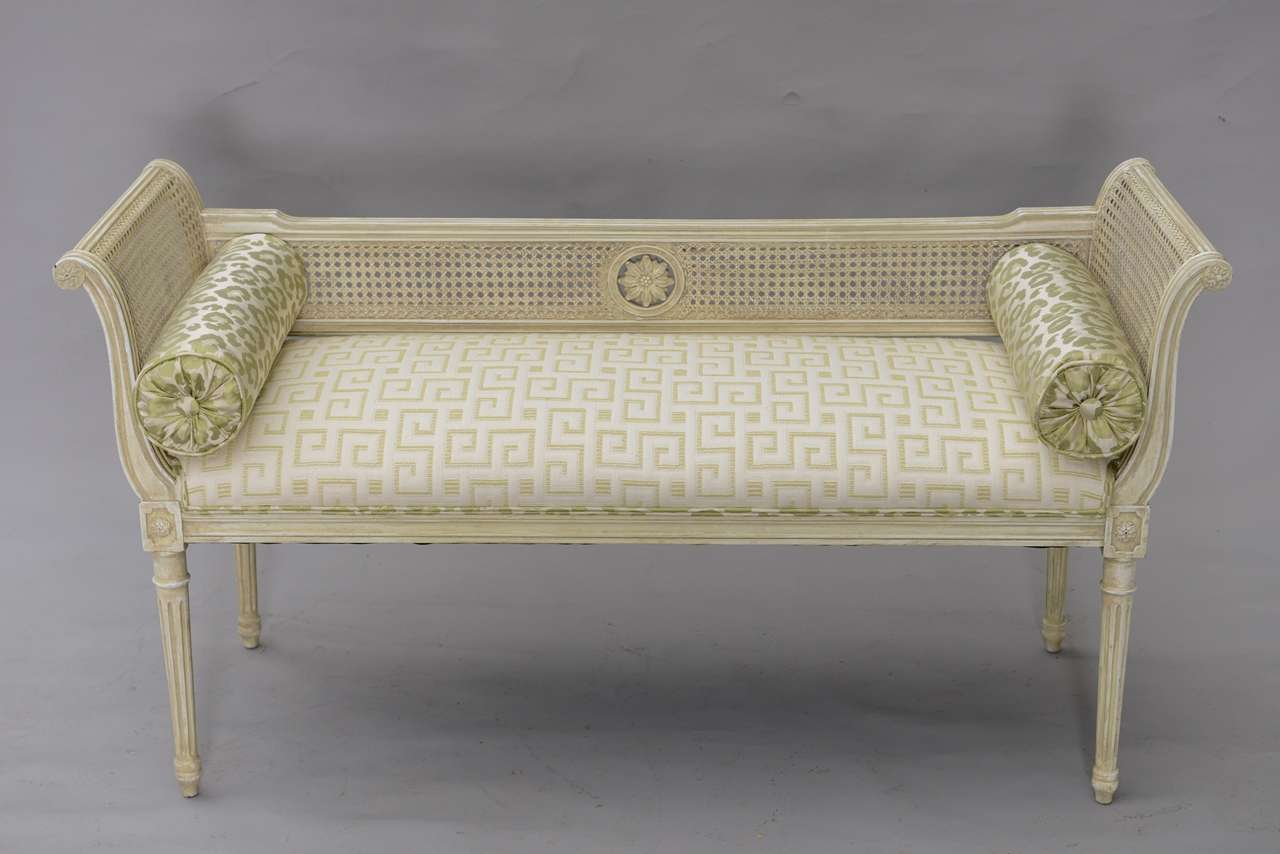 Window seat, having a distressed painted finish on its reeded frame, rectangular crown seat with low caned back centered with a rosette, flanked by caned scrolling arms, raised on rosette-headed, round fluted tapering legs, terminating in toupie